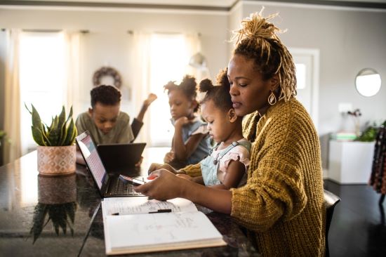 Mother working on a laptop while children engage with devices